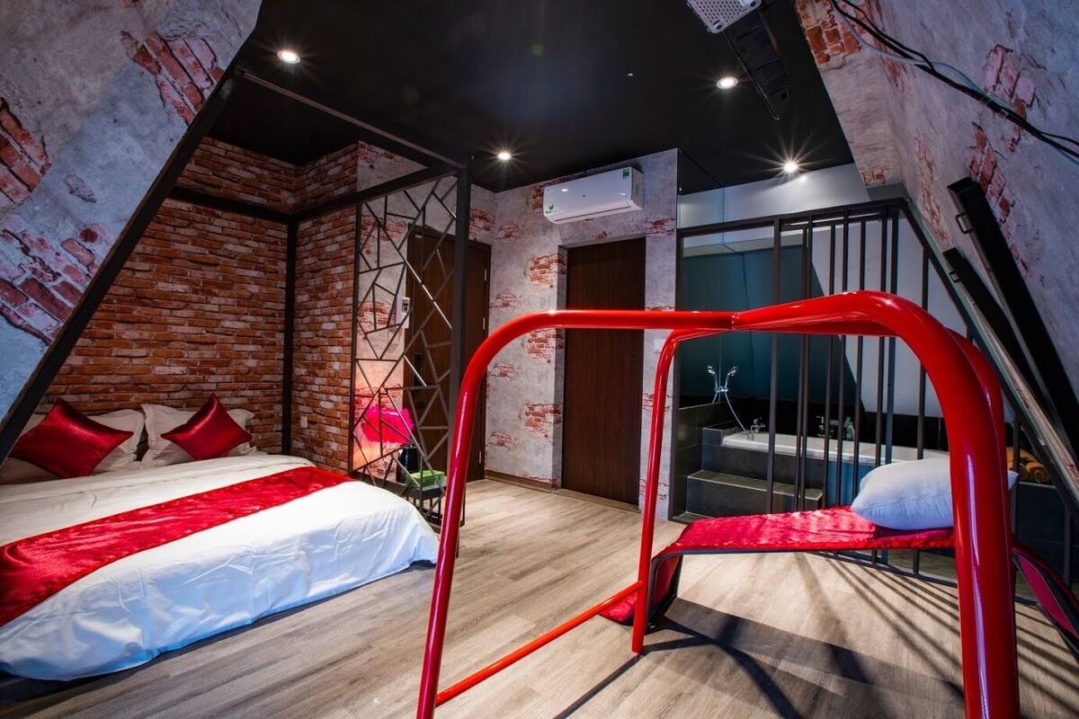Een moderne slaapkamer met een schuine plafond, openliggende bakstenen muren, een groot bed met rode en witte beddengoed en een rode metalen bedomranding.