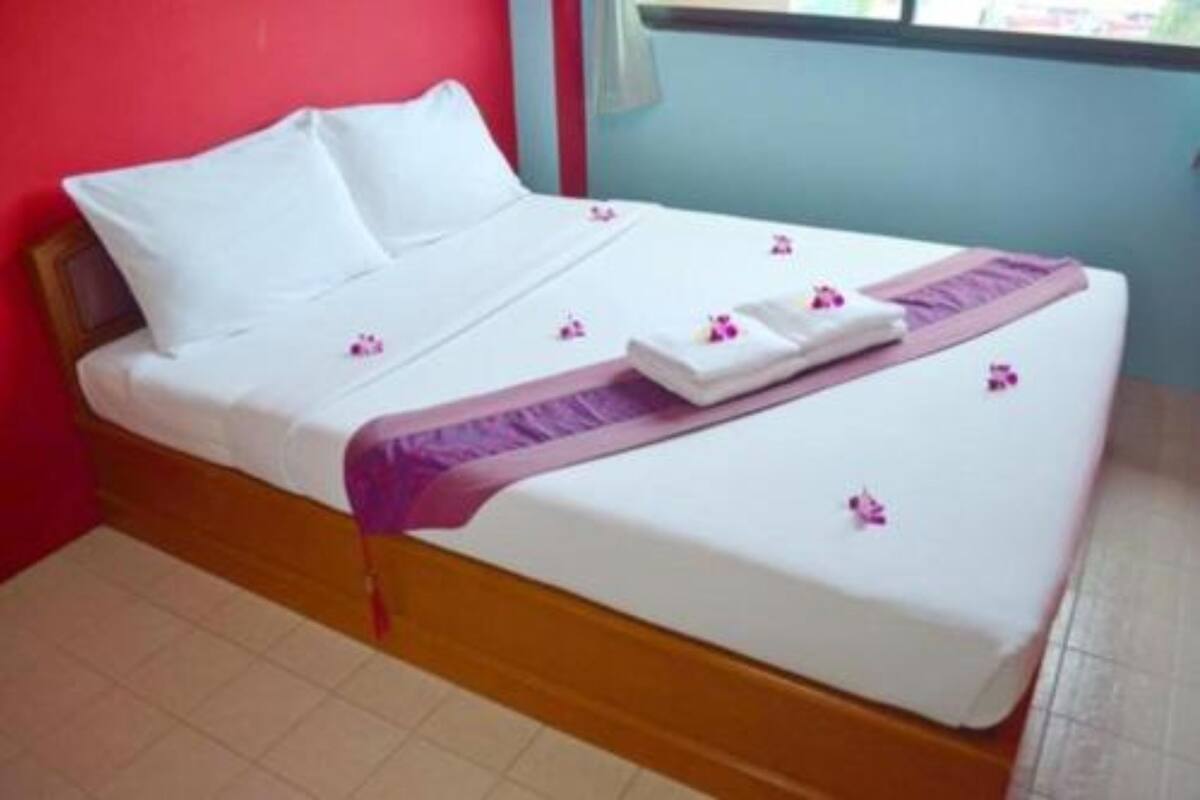 A neatly made bed with white linens, a purple throw blanket, and pink flower petals scattered on the bed.