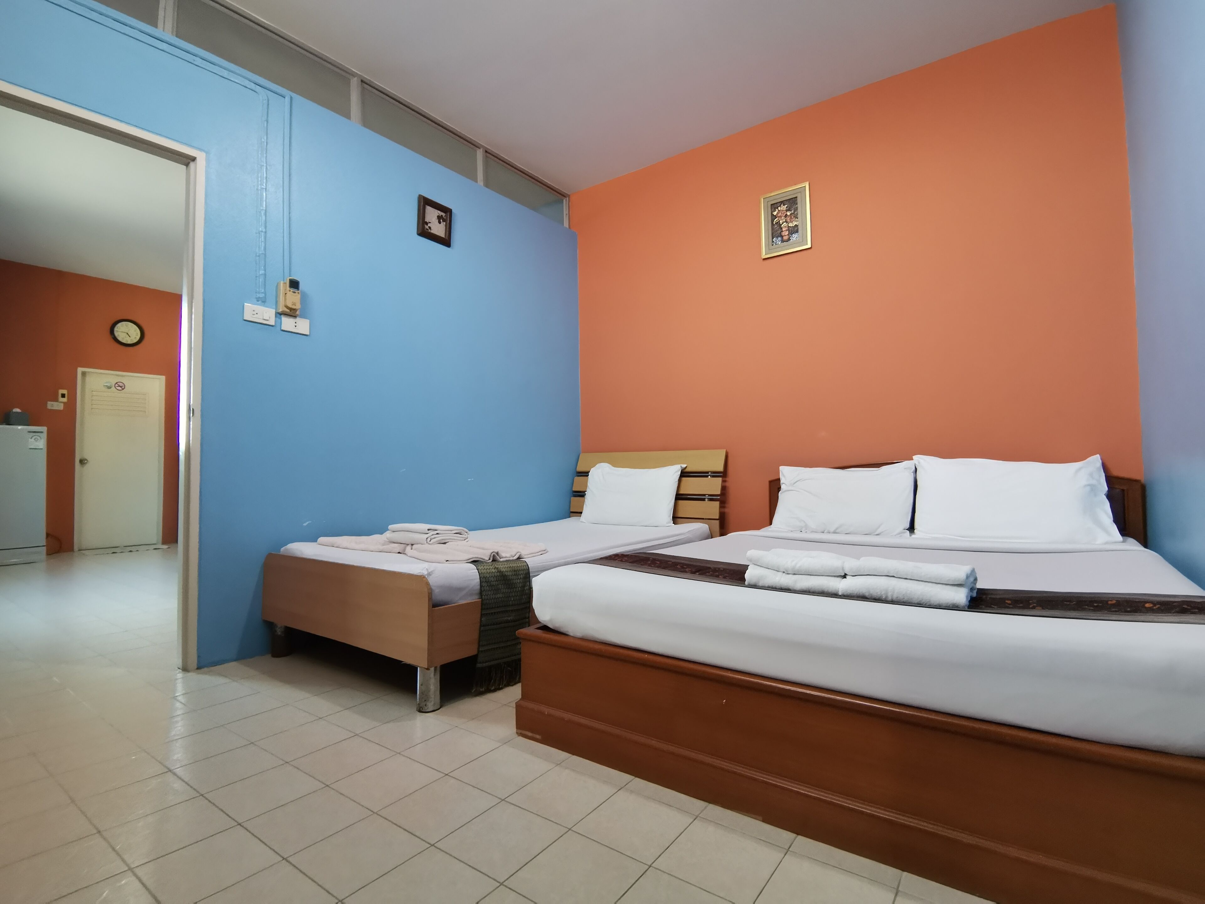 A hotel room with two beds, a blue wall, an orange wall, and a tiled floor.