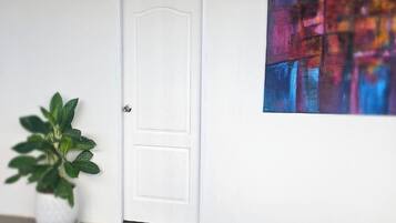 A waiting area with a white door, a potted plant, and a colorful abstract painting on the wall.