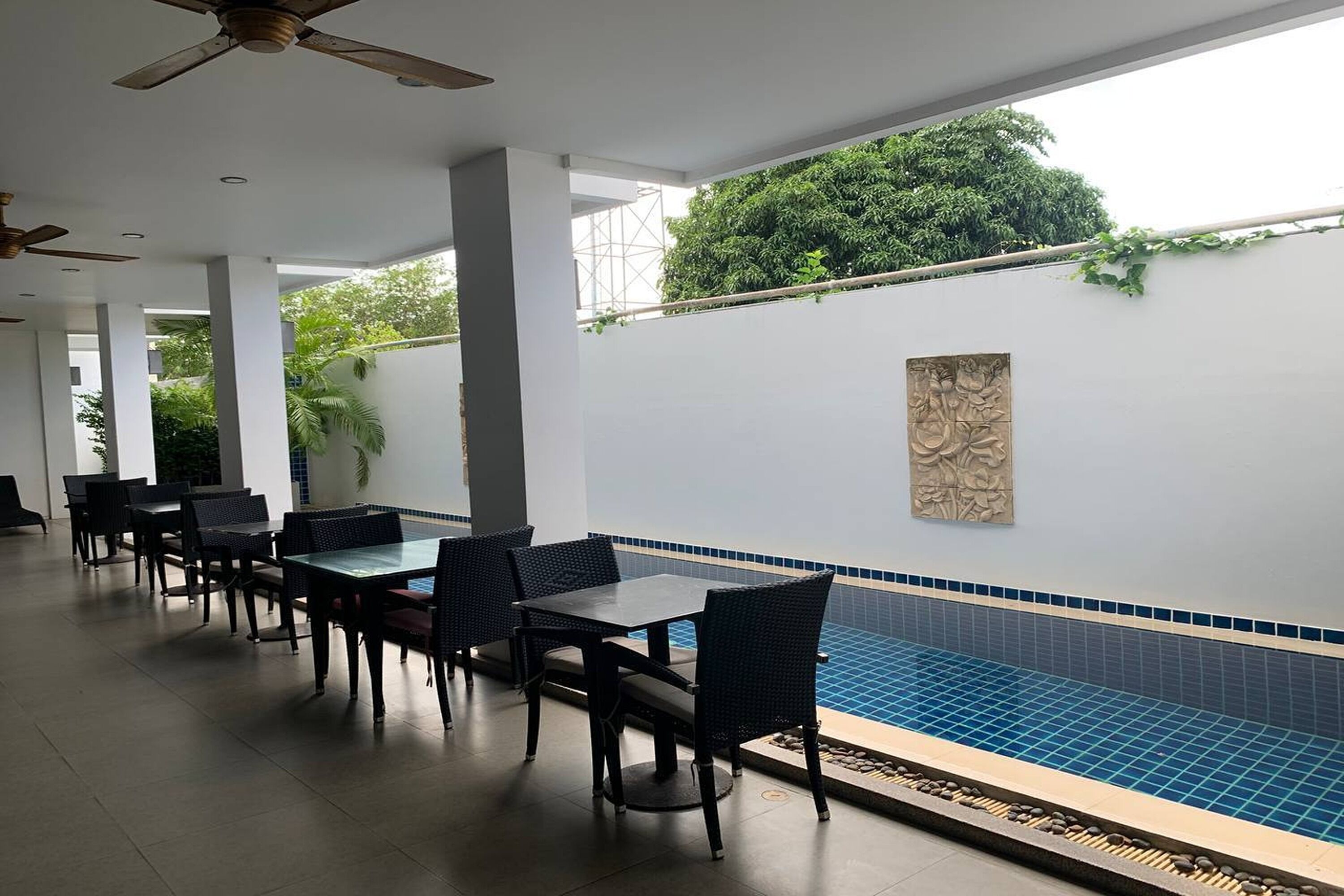 Un espace aménagé au bord de la piscine, avec des tables et des chaises, un ventilateur de plafond et un mur décoratif.