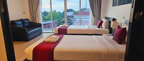 Habitación de hotel con dos camas, un sofá y un amplio ventanal con vistas a edificios y zonas verdes.