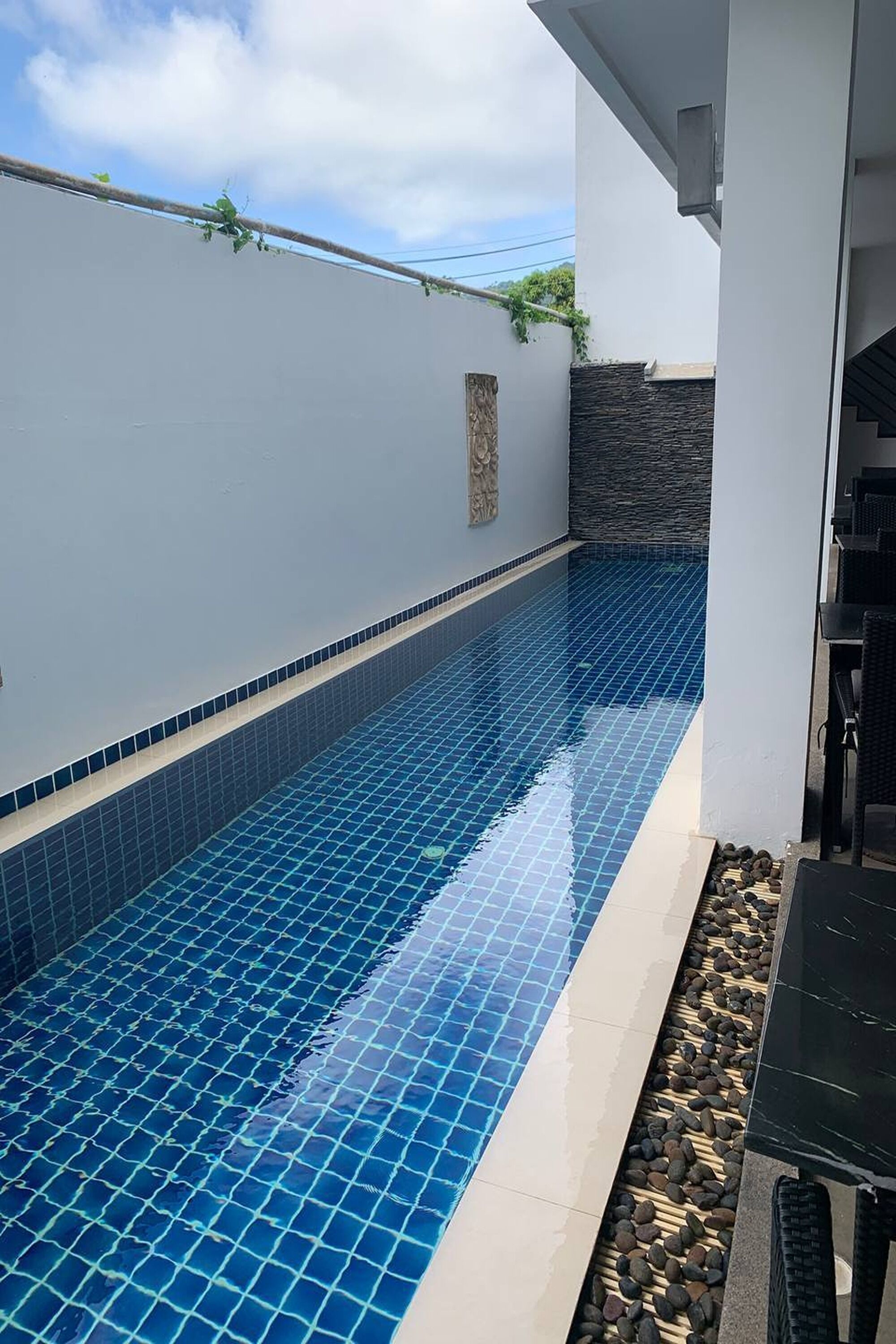 Ein Swimmingpool mit blauen Fliesen, einer Steinmauer und einem Grillbereich.