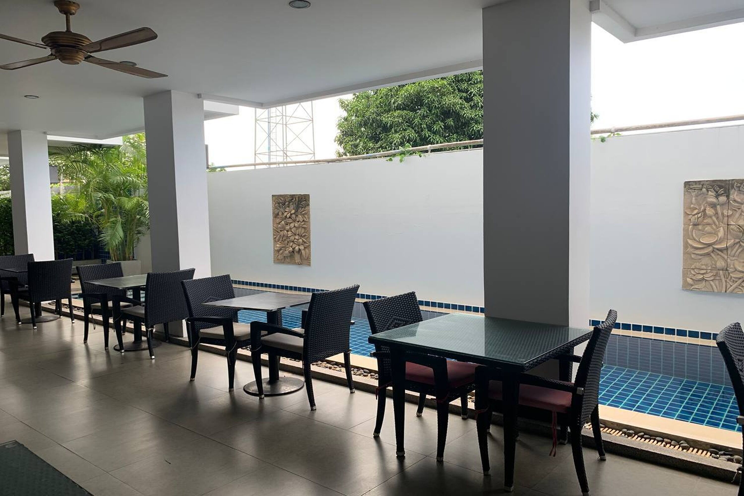 An outdoor dining area with tables and chairs, a ceiling fan, and a view of a swimming pool.