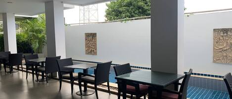 An outdoor dining area with tables and chairs, a ceiling fan, and a view of a swimming pool.
