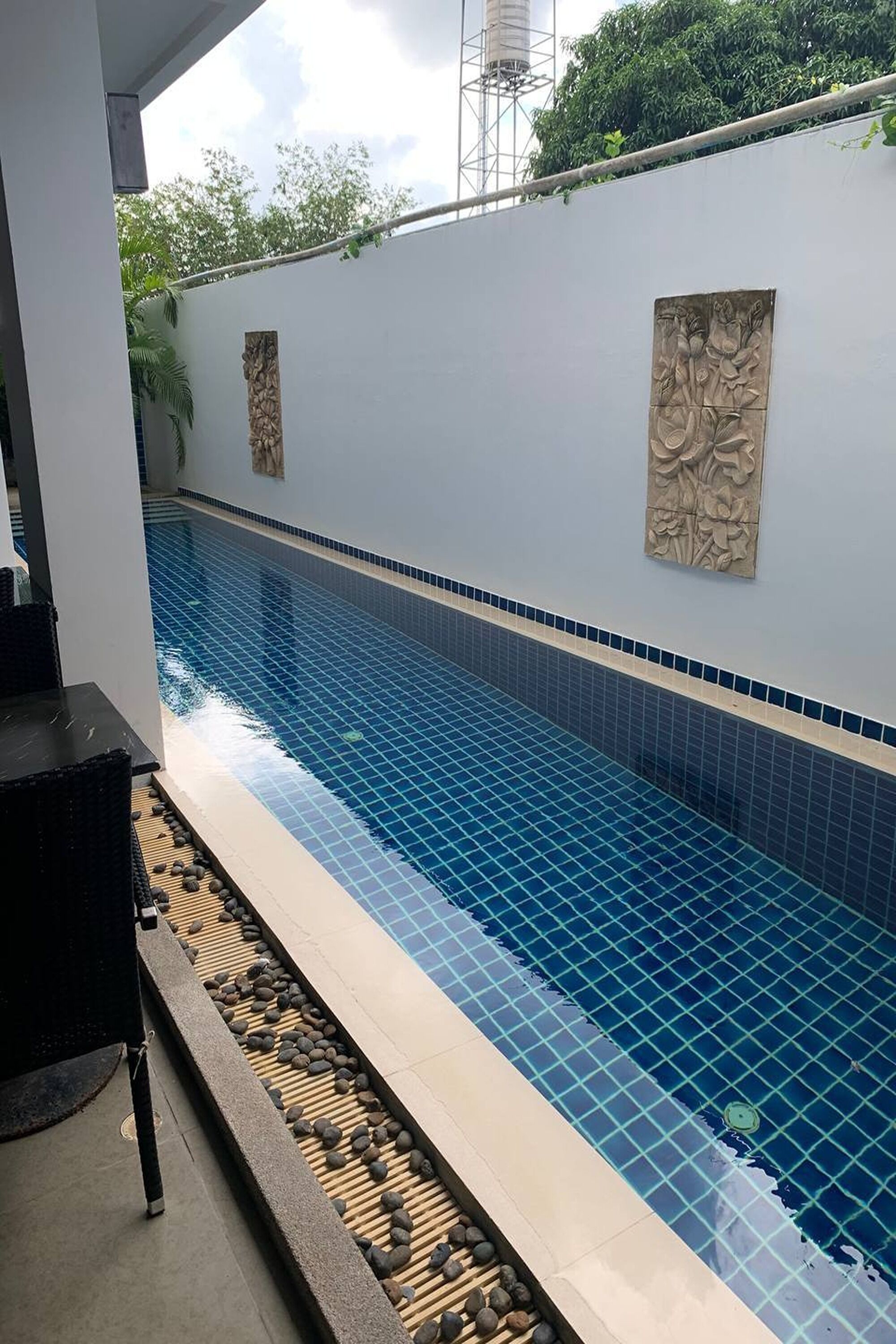 Ein Swimmingpool mit blauen Fliesen und dekorativen Wandverkleidungen, umgeben von einem mit Stein ausgekleideten Deck.