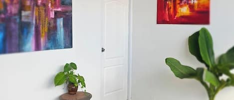 Une pièce avec un ventilateur de plafond, deux tableaux abstraits, une plante en pot et une porte.