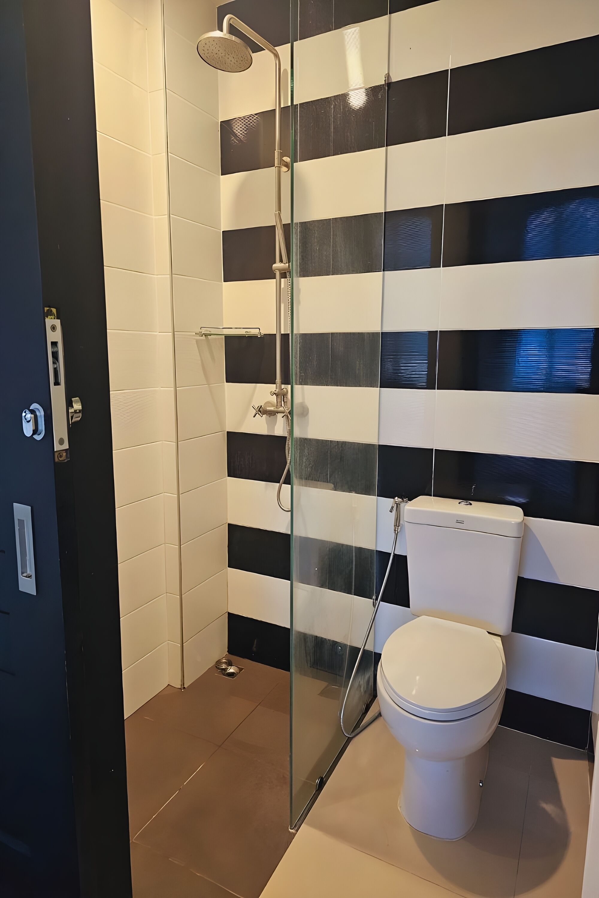 A bathroom with a glass-enclosed shower, a toilet, and a black and white tiled wall.
