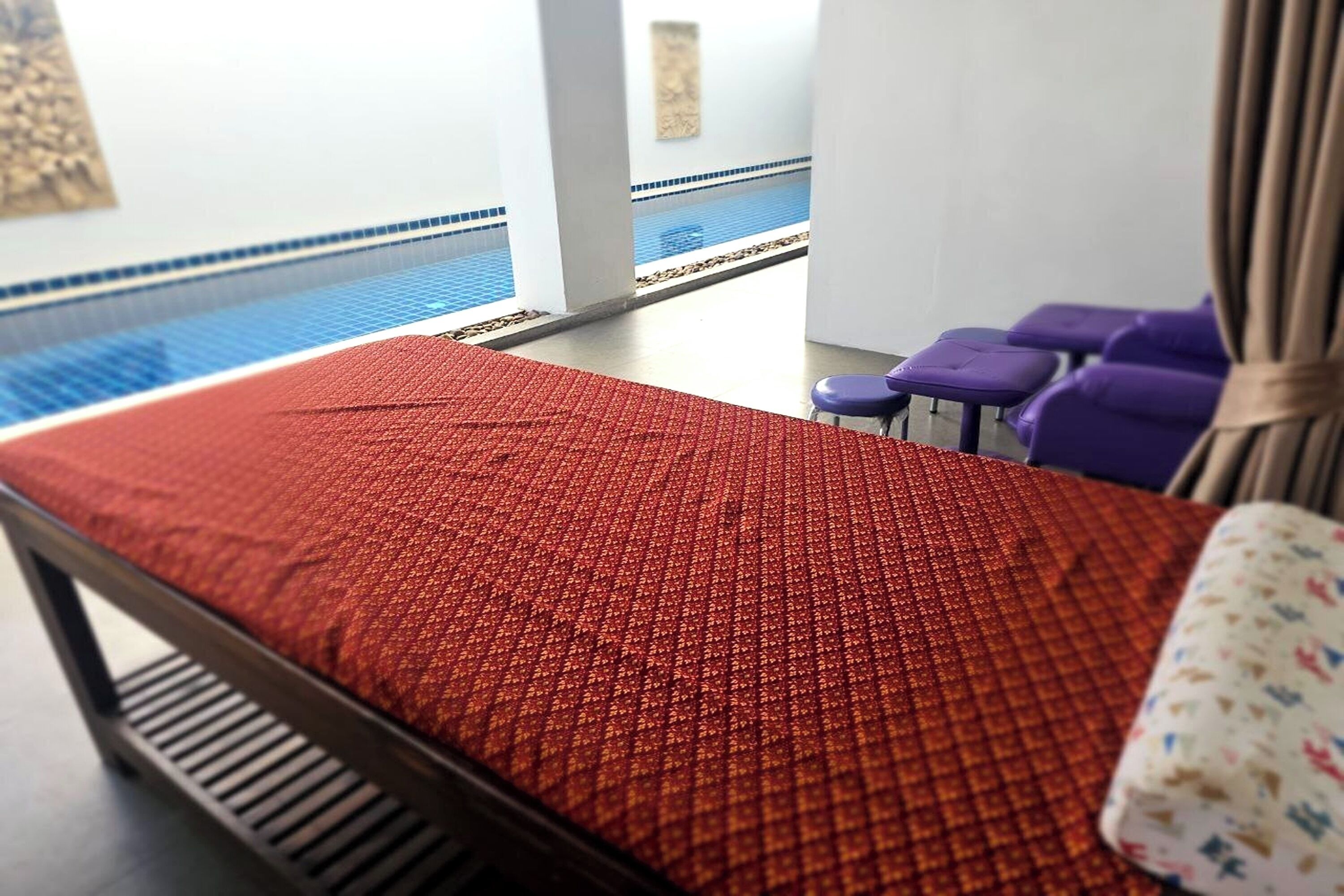 A hotel room with a red patterned bedspread, a view of a swimming pool, and purple chairs.