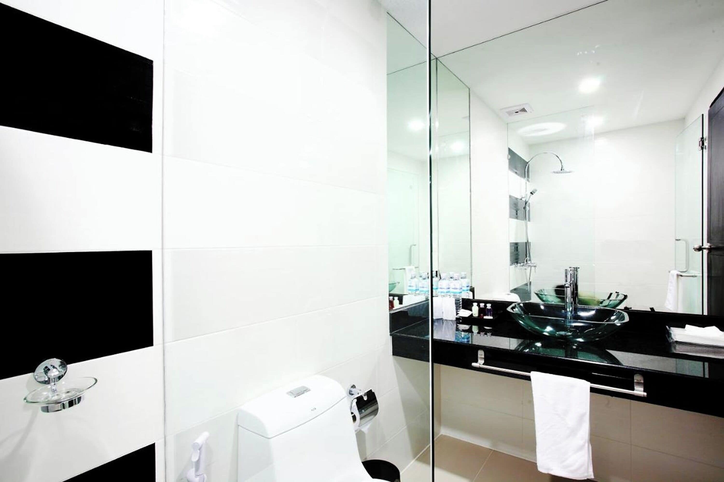 Un baño moderno con cabina de ducha de vidrio, encimera negra y toalla blanca colgada en la pared.