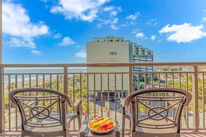 Enjoy a beachfront view from this balcony, featuring a comfortable seating area with a table and a basket of fresh fruit.
