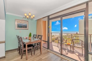 A balcony with a view of the ocean, a dining area with a table and chairs, and a chandelier.