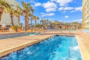 A swimming pool with palm trees, lounge chairs, and a clear blue sky.