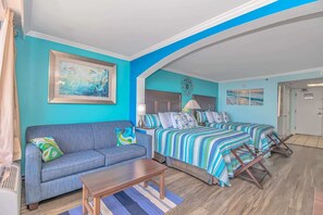 A room with a sofa, a bed with striped bedding, a framed picture on the wall, and a door in the background.
