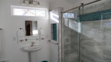 A modern bathroom with a glass shower enclosure, a white sink, and a mirror above it.