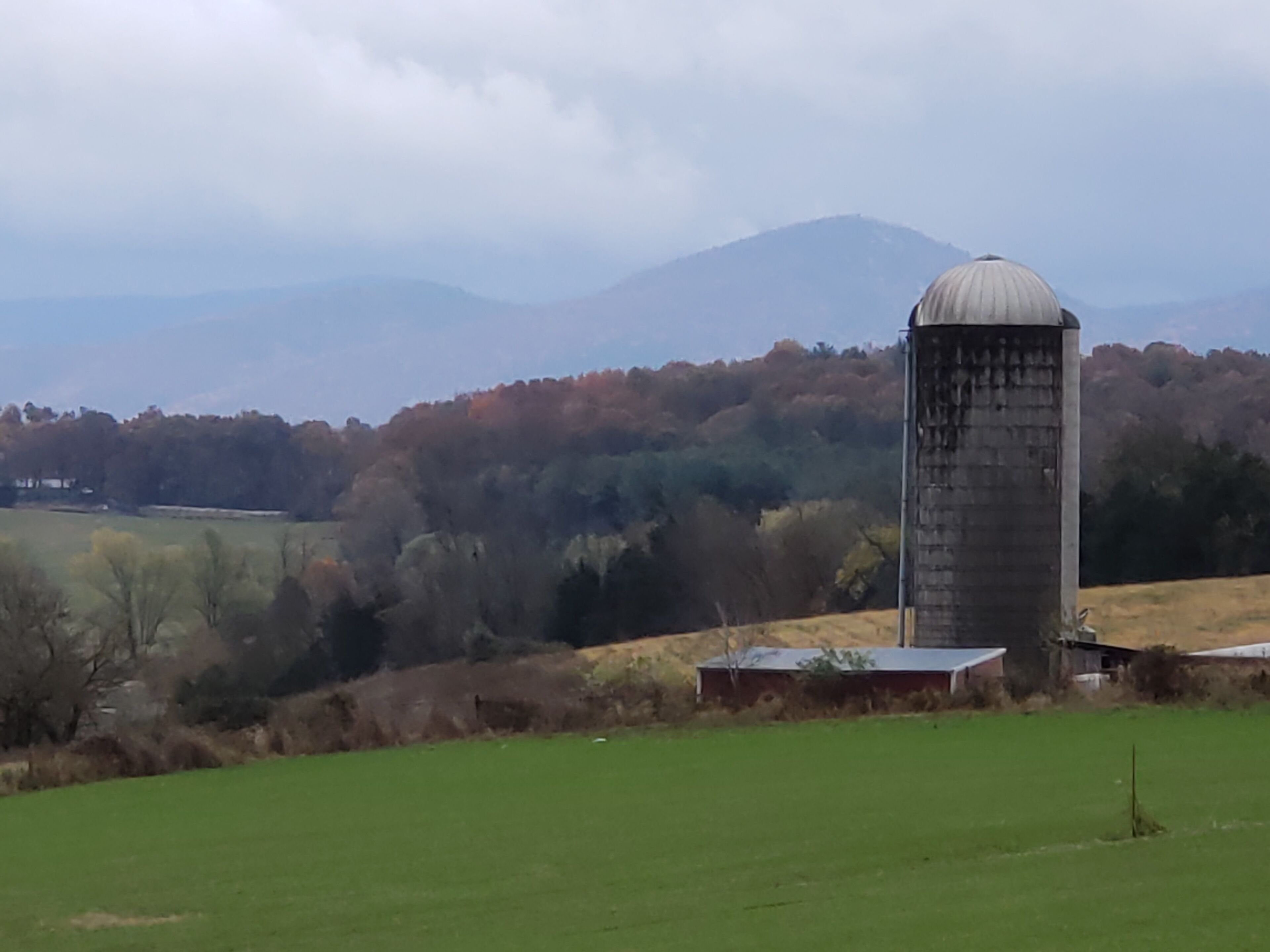 Paisaje rural con un silo y una construcción pequeña, rodeado de campos y árboles.