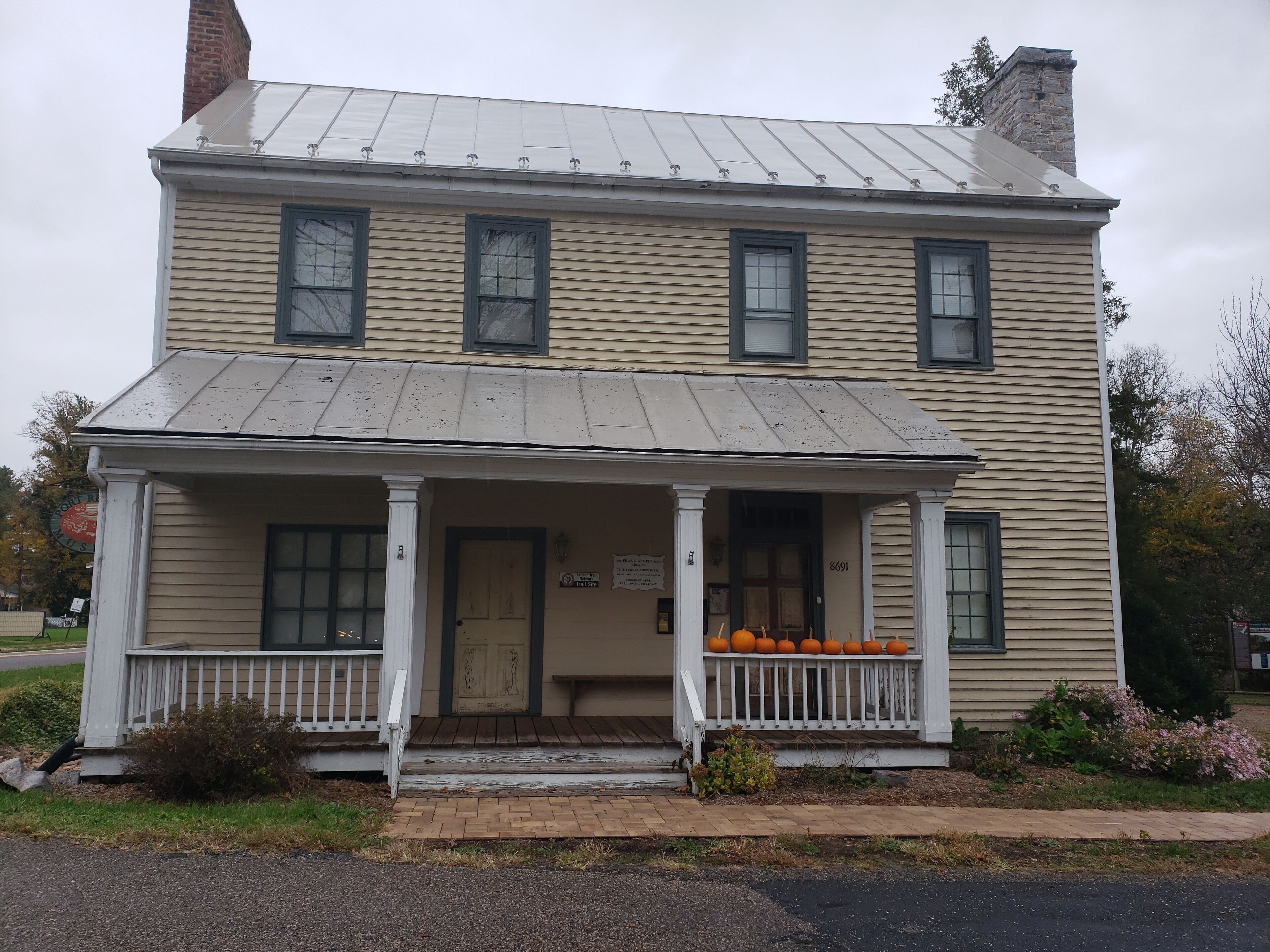 A two-story building with a porch, a chimney, and a sign indicating it is a historic site.