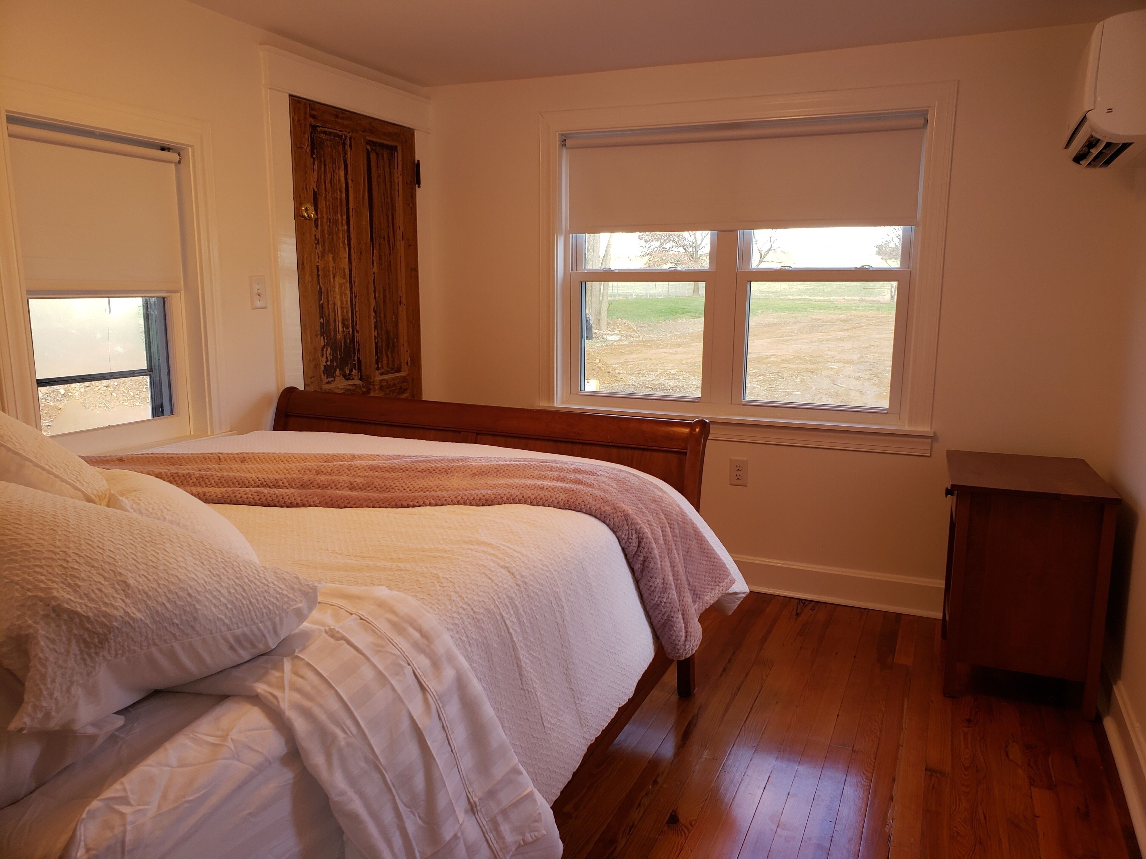 A bedroom with a wooden bed, a window with a view of the outdoors, and a small wooden nightstand.