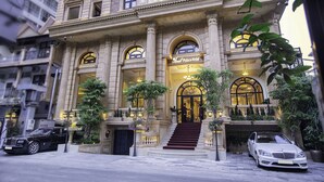 A grand hotel entrance with a marble facade, large arched windows, and a staircase leading to the entrance.