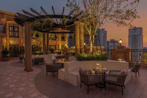 A rooftop terrace with outdoor seating, columns, and hanging plants.