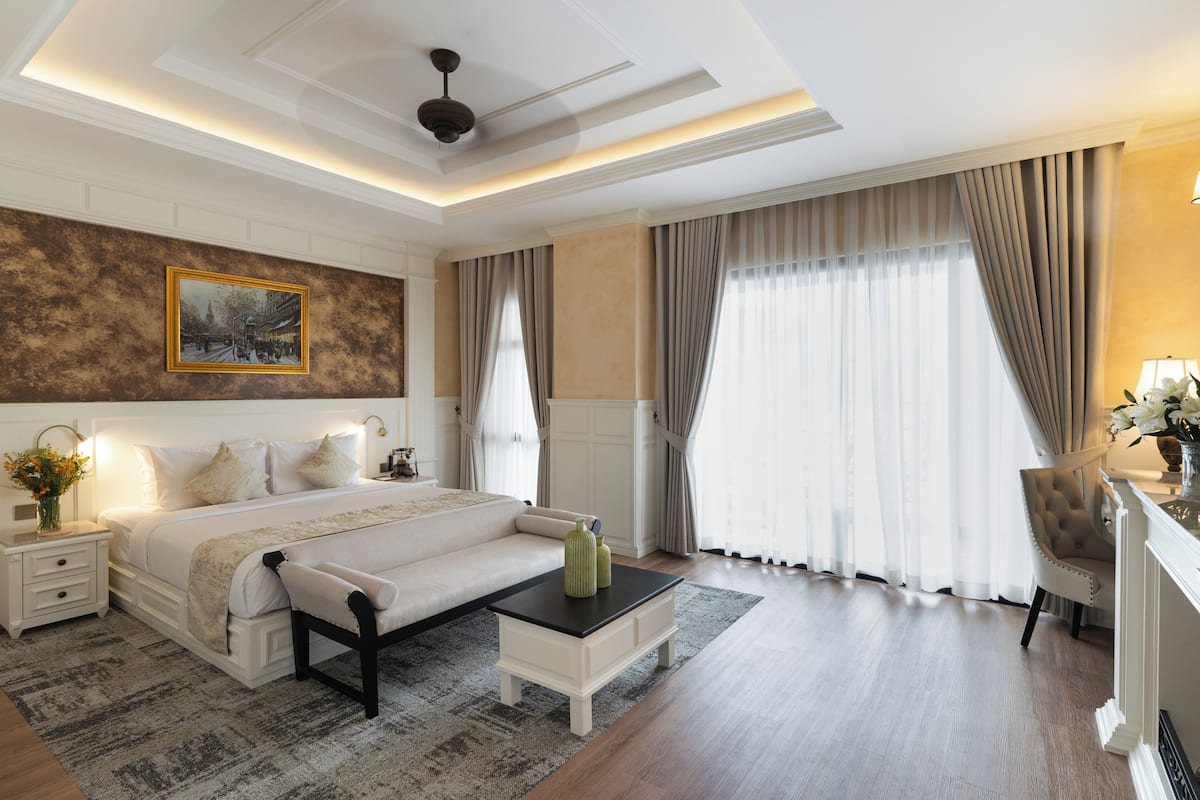 Quarto moderno com uma cama grande, mesas de cabeceira, um banco, uma mesinha e um quadro na parede.