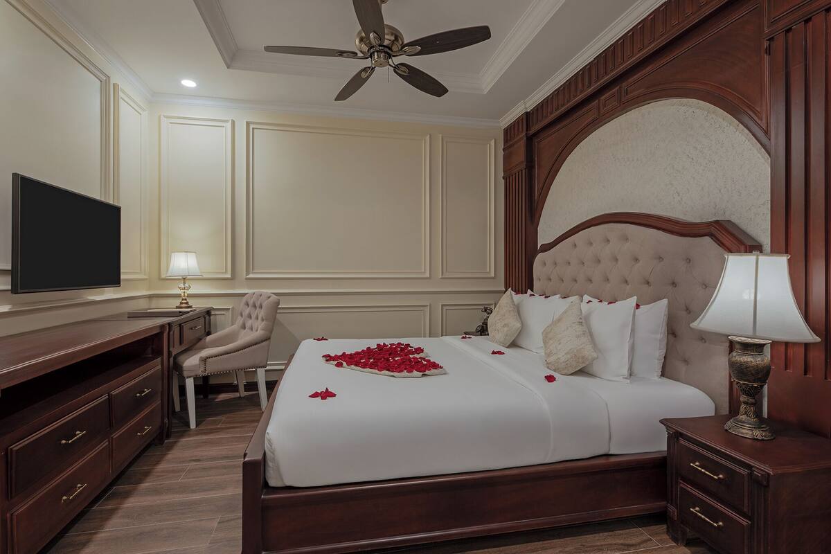 Quarto de hotel com uma cama grande, televisão, escrivaninha e uma cadeira.