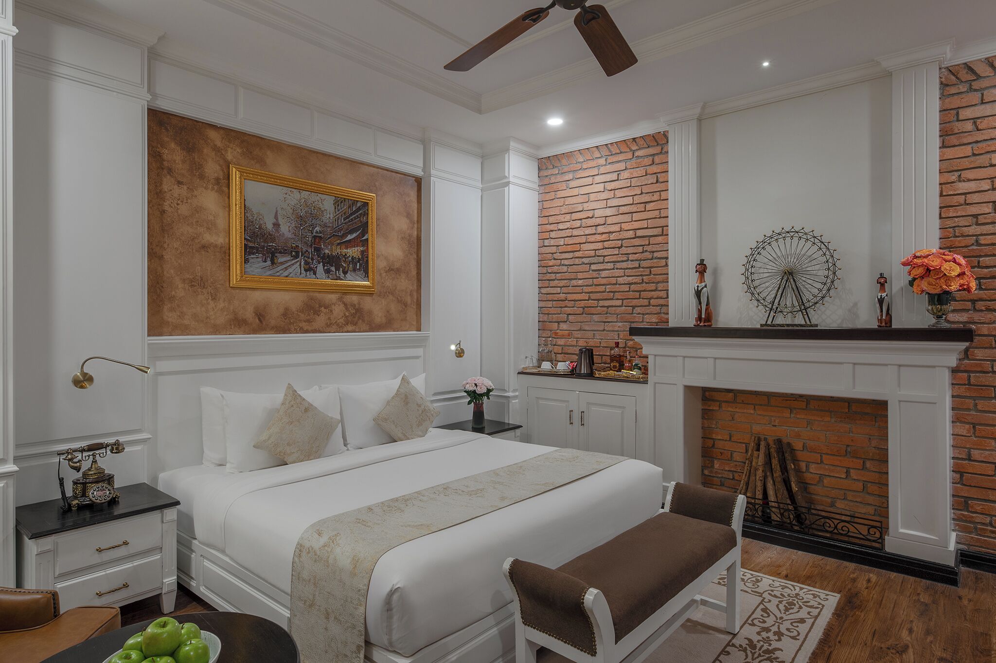 Un dormitorio con una cama grande, chimenea, pared decorativa de ladrillo y ventilador de techo.