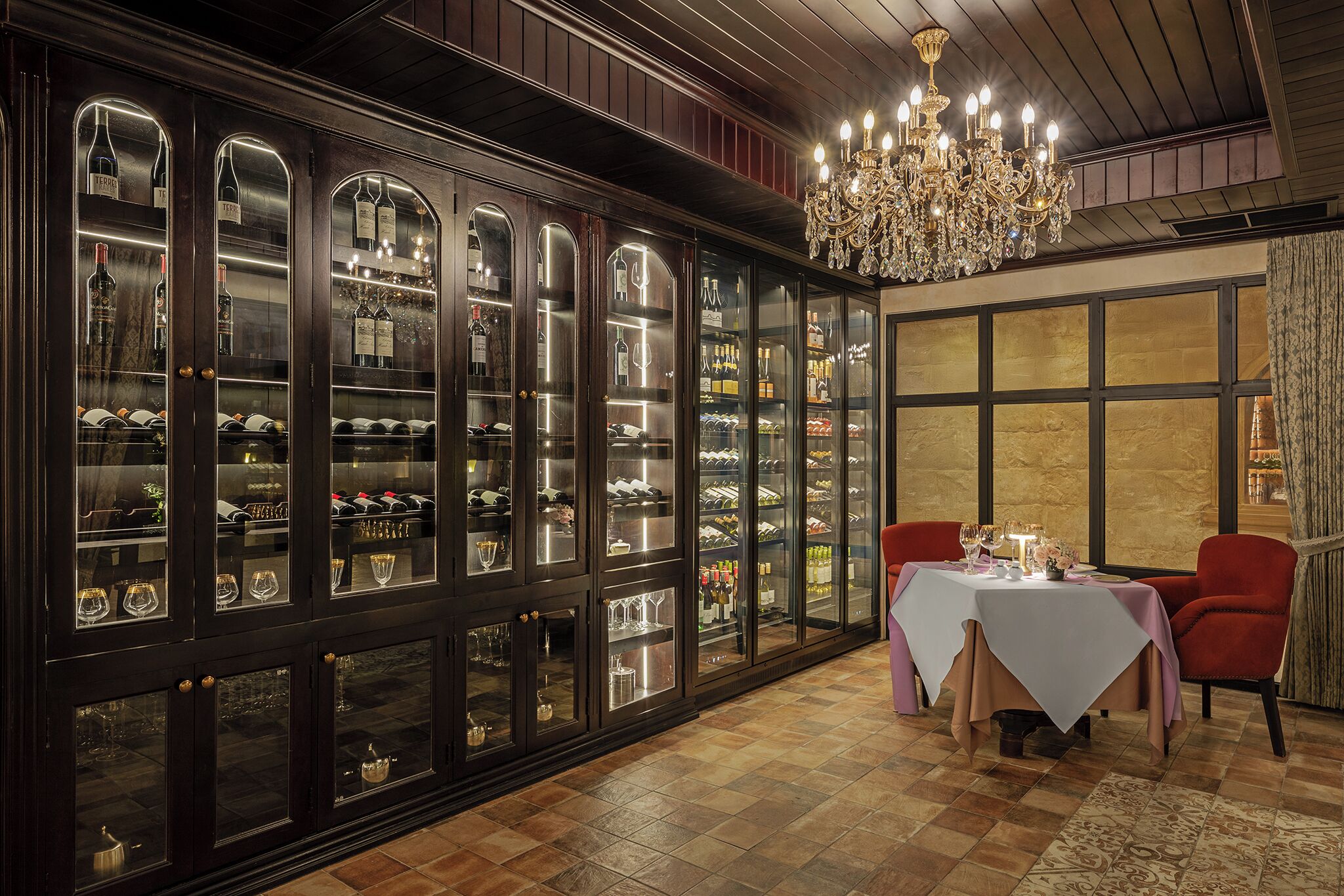 A room with a large wine cabinet, a chandelier, and a table set for dining.