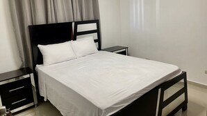 A bedroom with a bed, a nightstand, a small table, and a window with curtains. - 3 Bedroom Apartment with Resort like Pool (Stgo)