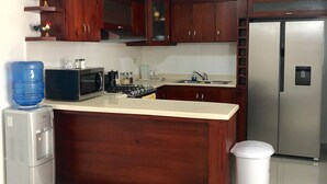 A kitchen with wooden cabinets, a stainless steel refrigerator, a microwave, and a water dispenser. - 3 Bedroom Apartment with Resort like Pool (Stgo)