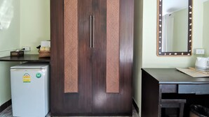 Une chambre avec une armoire en bois foncé, un petit réfrigérateur, un bureau avec un miroir et une poubelle.
