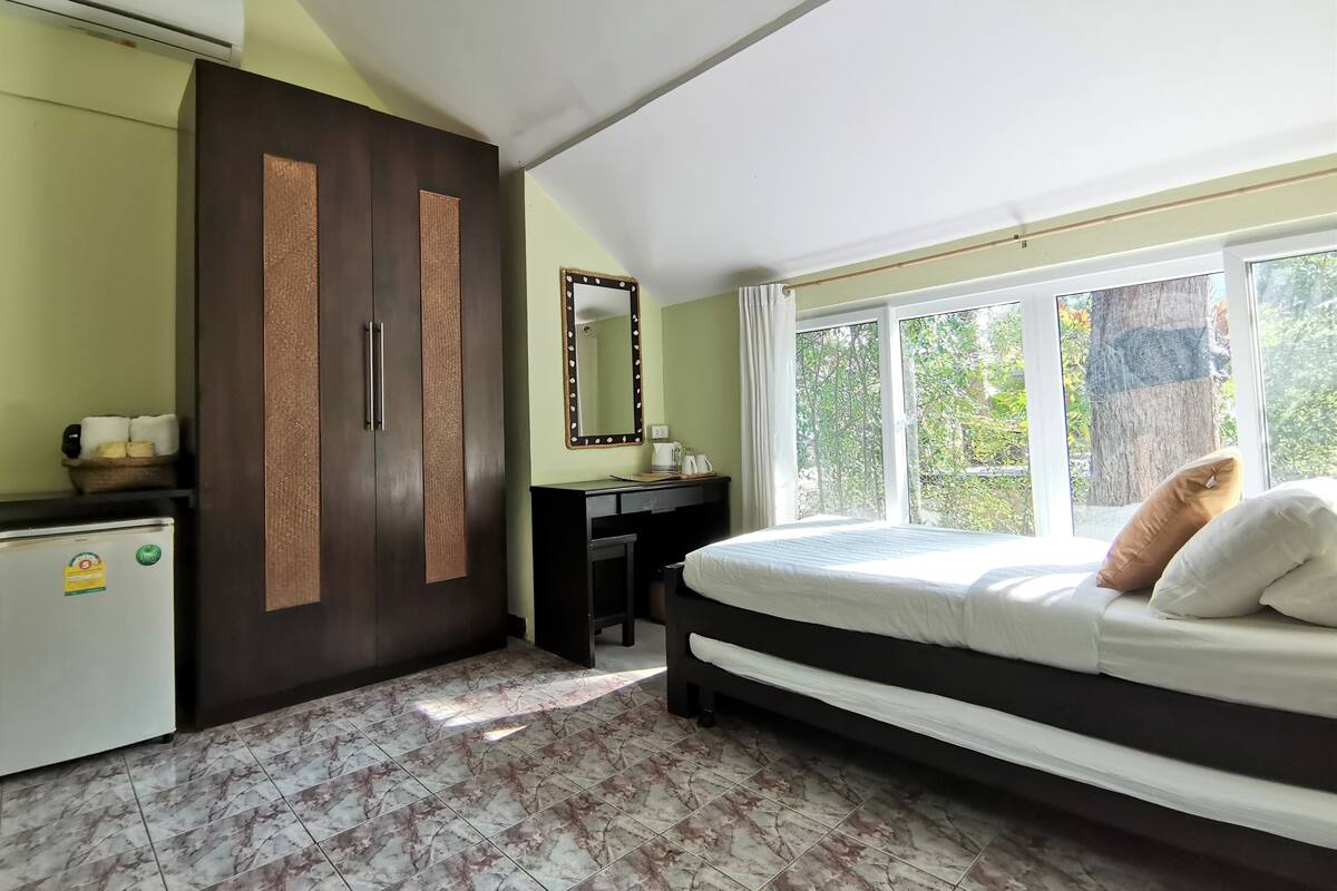 Een slaapkamer met een bed, een bureau, een kledingkast en een groot raam.