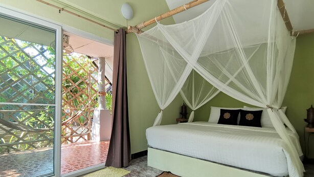 Une chambre avec un lit, une moustiquaire, une fenêtre et une vue sur la verdure environnante.