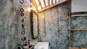 Une salle de bain avec un mur en marbre, une étagère en bois avec un distributeur de savon et un lavabo blanc.