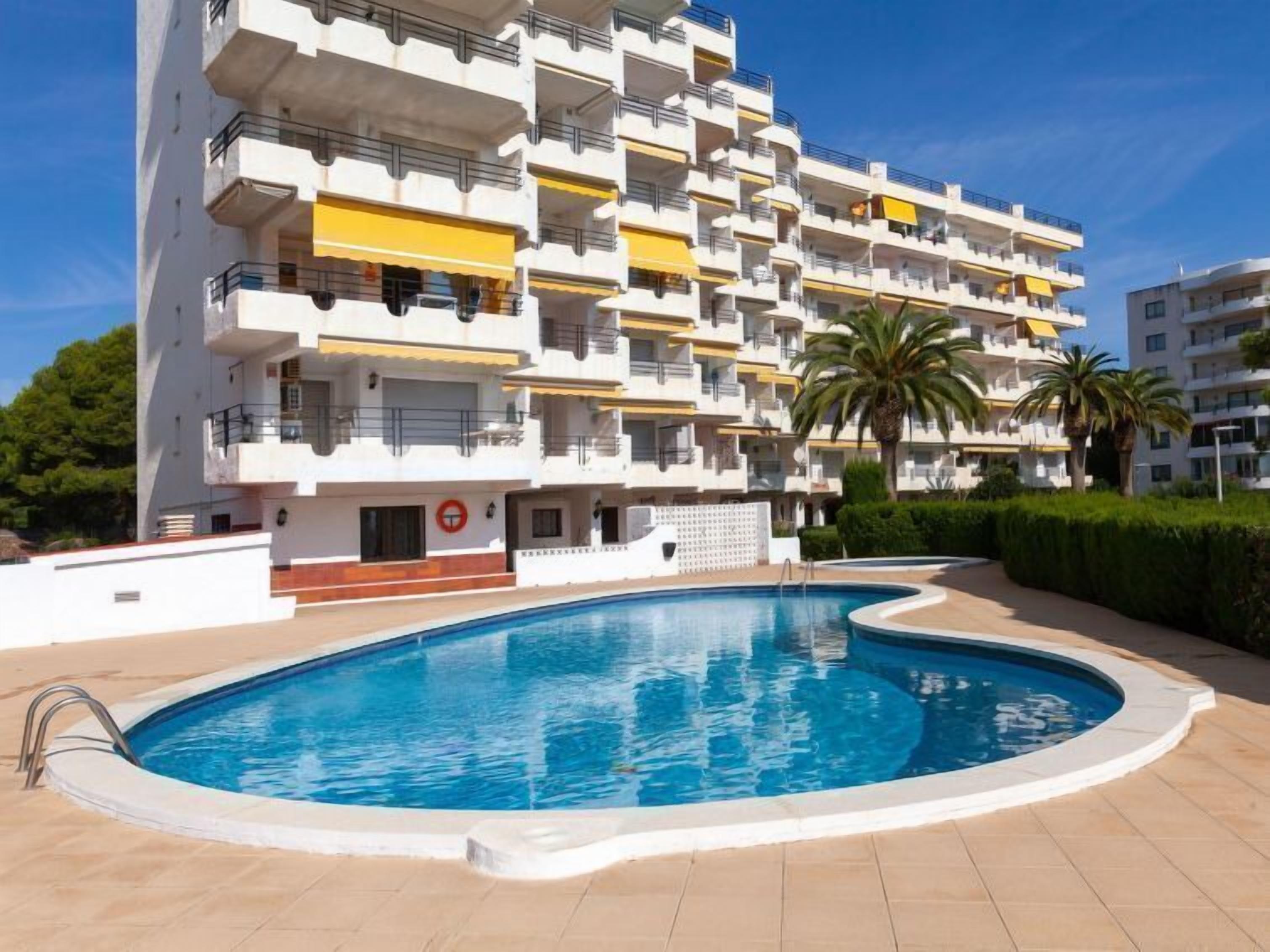 Un edificio residencial de varios pisos con balcones, piscina y palmeras.