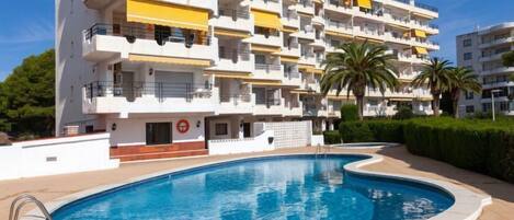 Un edificio residencial de varios pisos con balcones, piscina y palmeras.