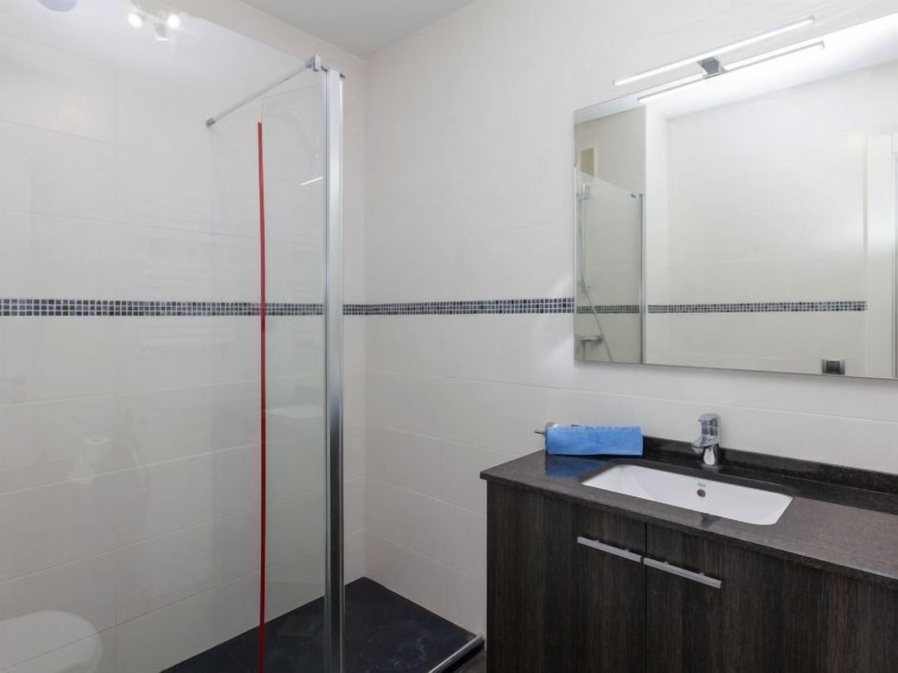 Un baño moderno con cabina de ducha de vidrio, un mueble de tocador de madera oscura con lavabo blanco y un espejo sobre el mueble.