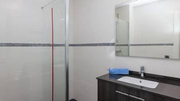 Un baño moderno con cabina de ducha de vidrio, un mueble de tocador de madera oscura con lavabo blanco y un espejo sobre el mueble.