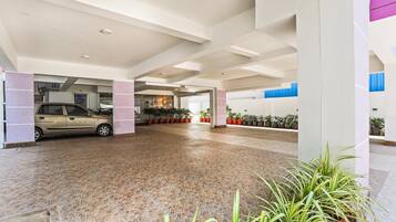 A spacious indoor area with a car parked in a covered section, surrounded by potted plants and a tiled floor.