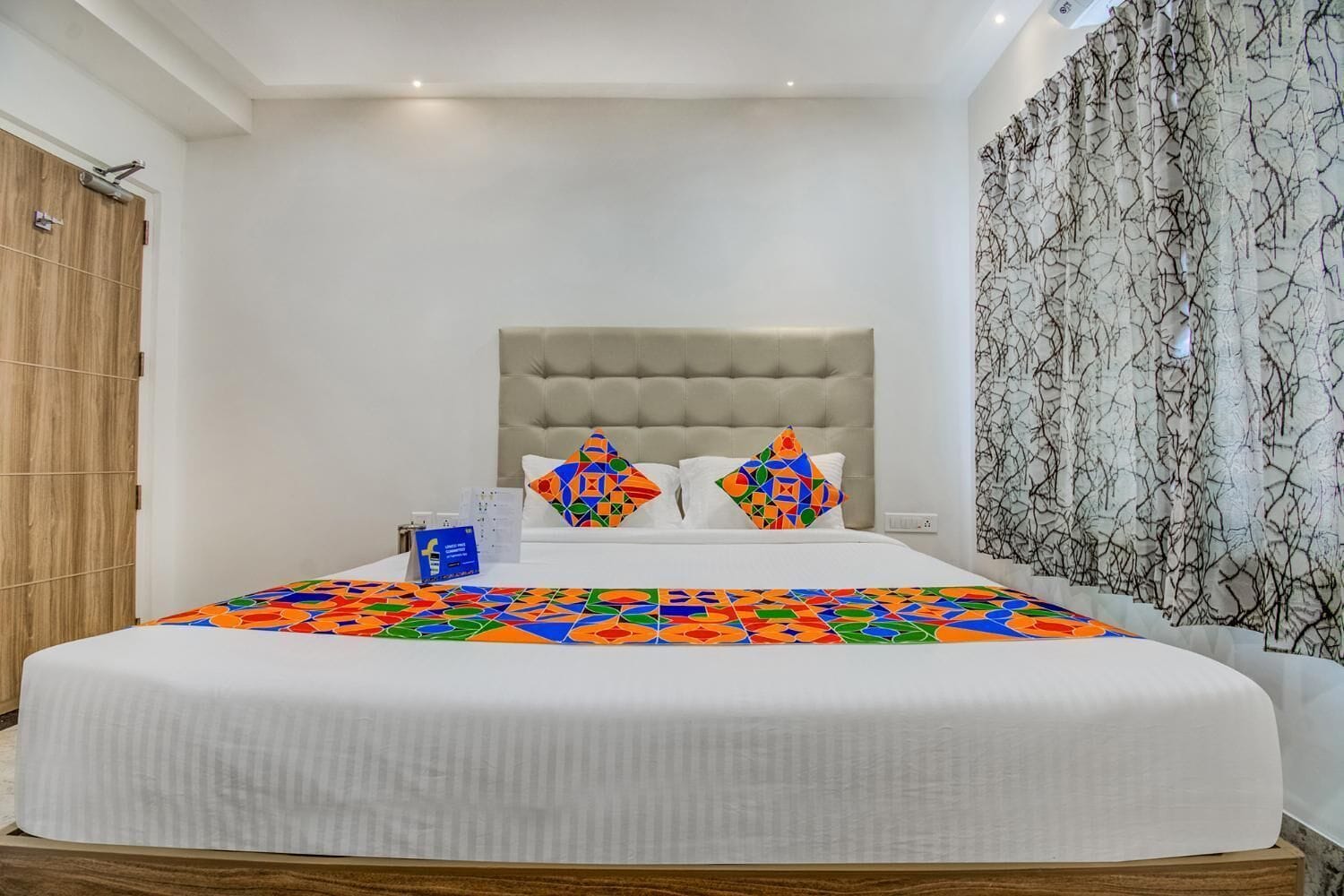 A neatly made bed with a white duvet, two decorative pillows, and a colorful geometric-patterned bedspread.