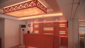 Een receptiebalie met een houten afwerking, een klok aan de muur en een modern verlichtingsplan.