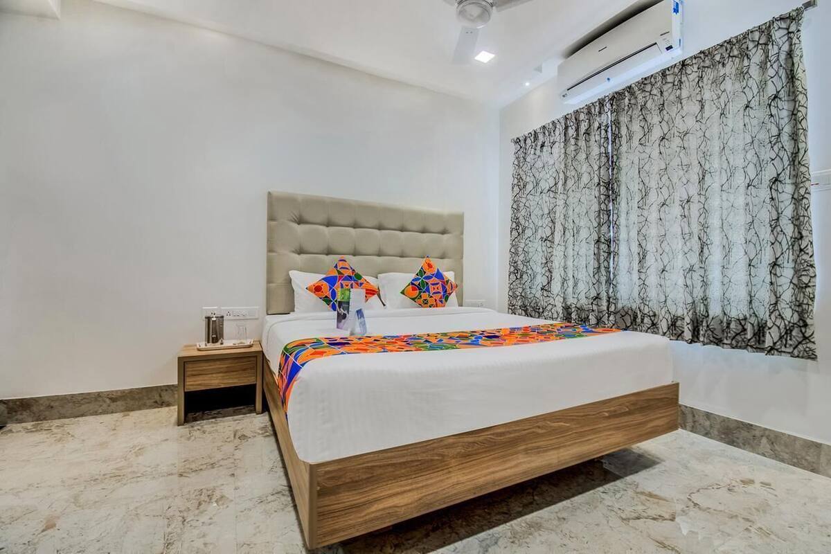 A bedroom with a bed, a nightstand, a wall-mounted air conditioner, and a patterned curtain.