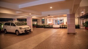 Ruime binnenruimte met een witte auto op de voorgrond, potplanten en een zithoek met een bank en tafel.