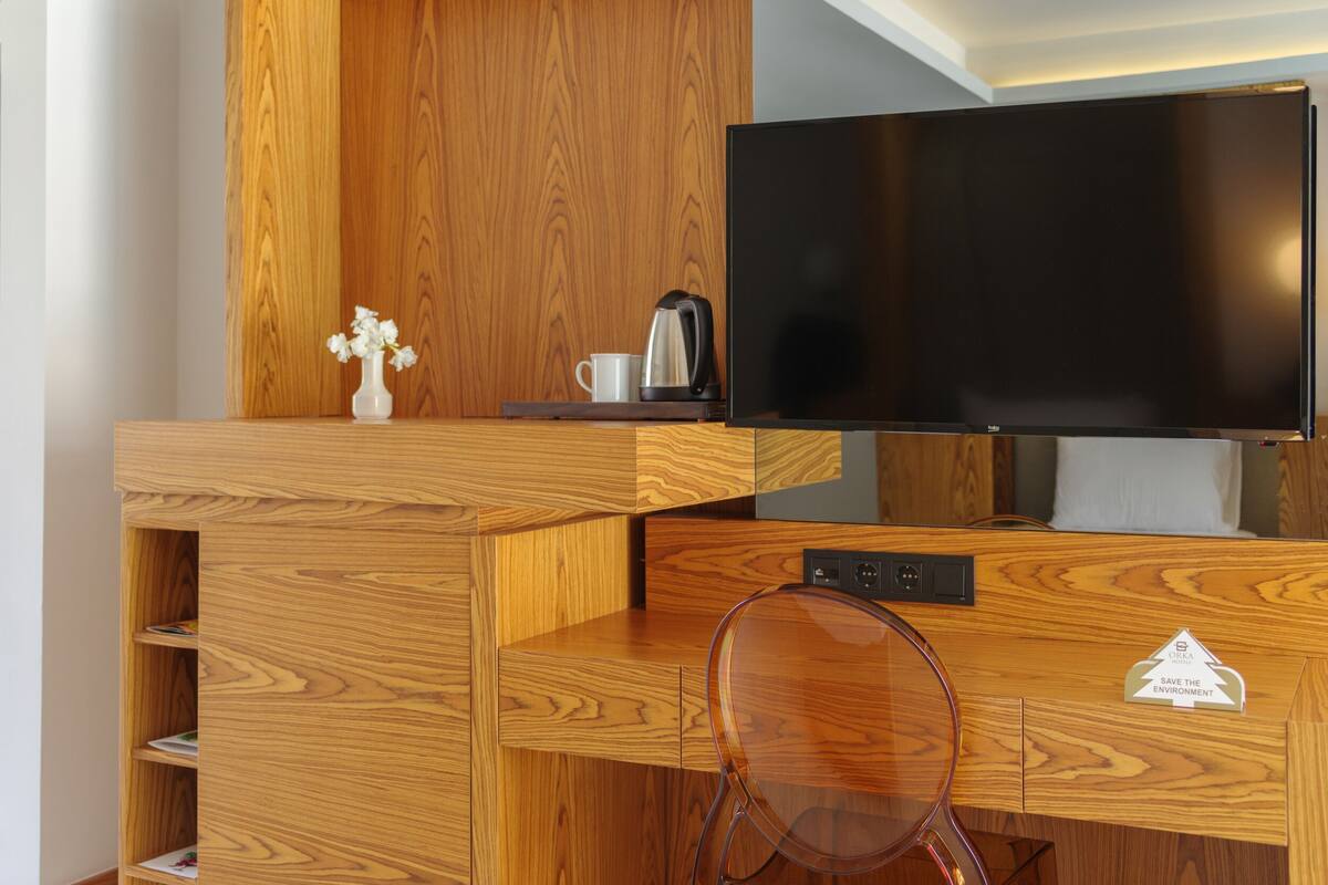 Un escritorio de madera con un televisor, un hervidor y un pequeño florero con flores.