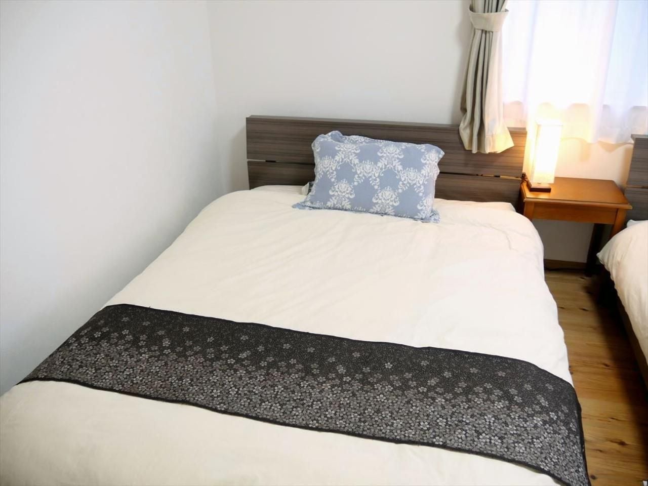 Un letto singolo con una coperta a fantasia, un cuscino e un comodino con una lampada.