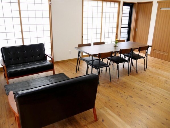 A room with a wooden floor, a black sofa, a dining table with chairs, and a sliding door.