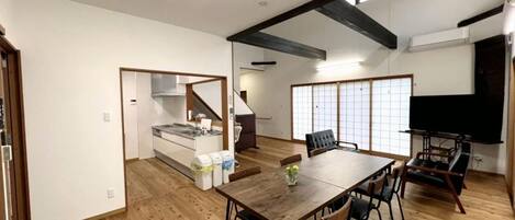A spacious living area with a wooden floor, a dining table, and a kitchen in the background.