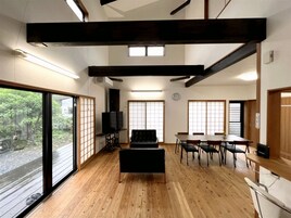 Una habitación amplia con suelo de madera, un sofá negro, una mesa de comedor con sillas y ventanas grandes que dejan entrar luz natural.