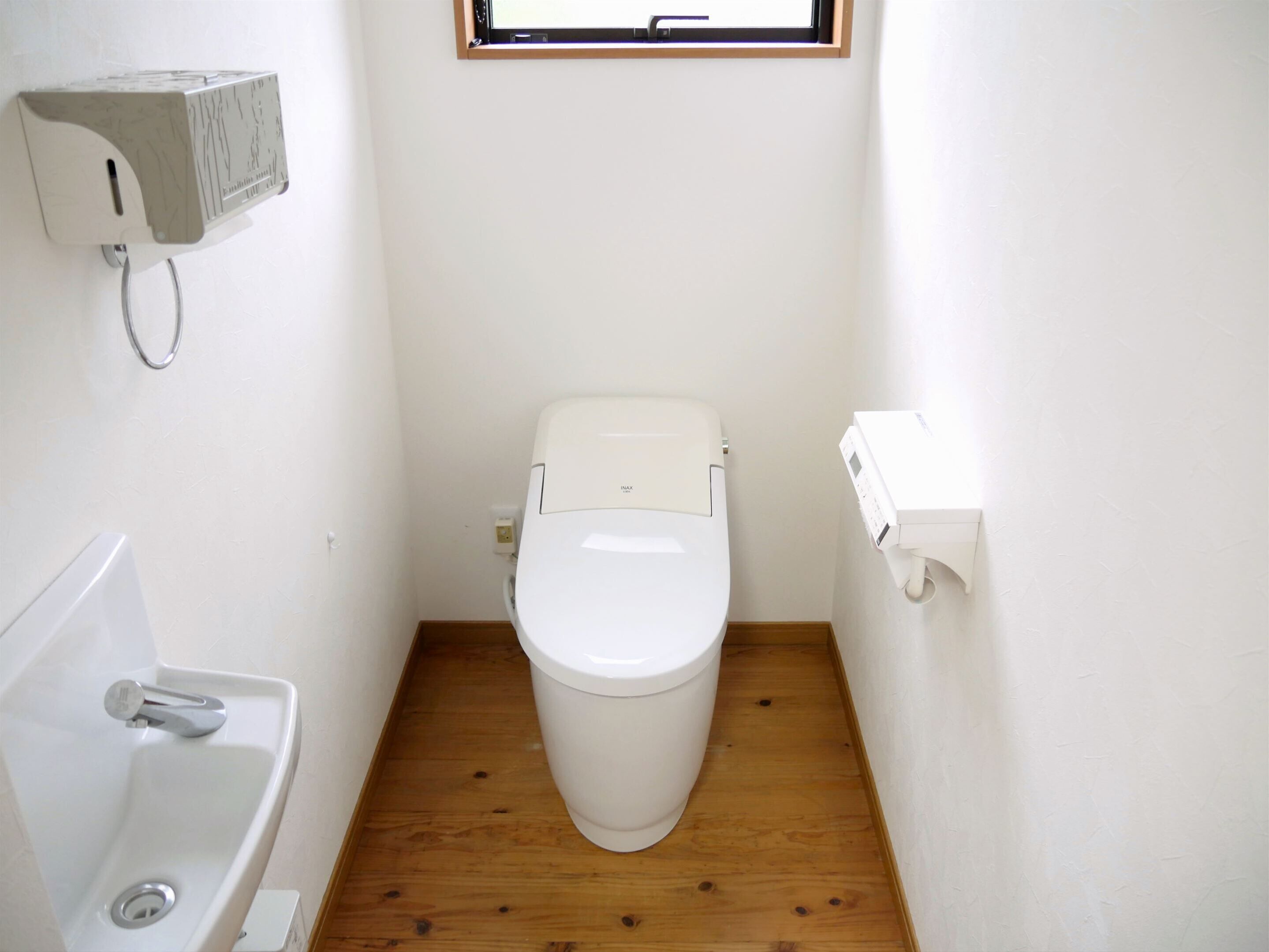 A small, compact bathroom with a white toilet, a sink, and a window above the toilet.