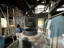Un interior rústico de madera con una gran estructura circular de piedra en el centro, posiblemente un pozo o una fuente.